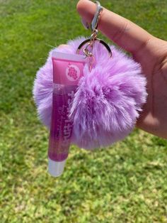 a person is holding up a pink lip bale with a keychain attached to it