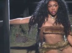 a woman with long black hair and no shirt is dancing in the rain while wearing fur