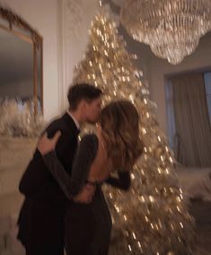 a man and woman are kissing in front of a christmas tree with lights on it