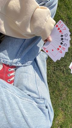 someone is holding playing cards in their pocket while sitting on the grass and looking down at them