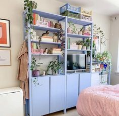 a bed room with a neatly made bed and a blue book shelf filled with plants