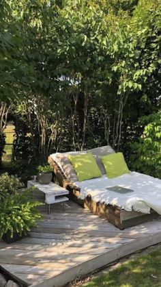 an outdoor lounge with pillows on it in the middle of some trees and grass area