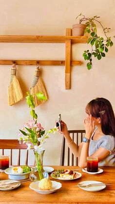 a woman sitting at a table with food and drinks in front of her, taking a photo