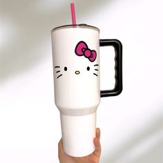 a hand holding a white hello kitty coffee cup with a pink straw sticking out of it