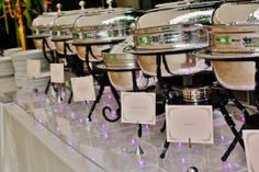 there are many plates and bowls on the table with purple lights around them, along with place cards