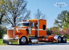 an orange semi truck is parked on the side of the road with trees in the background