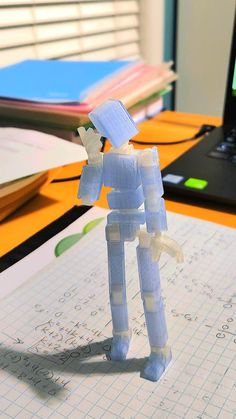 a plastic robot standing on top of a piece of paper next to a laptop computer