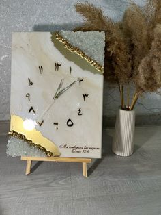 a white clock sitting on top of a table next to a vase filled with dry grass