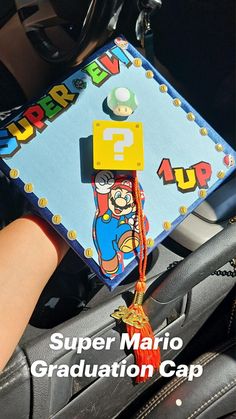 a hand holding a graduation cap with the word super mario on it and an orange tassel