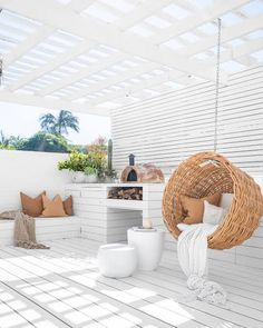 an outdoor living area with white walls and wood flooring, large wicker hammock hanging from the ceiling