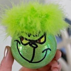 a hand holding an ornament with a green face and yellow hair on it