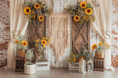 an arrangement of sunflowers and greenery on display in front of a rustic backdrop