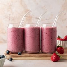 three smoothies with strawberries and blueberries on a cutting board next to bowls