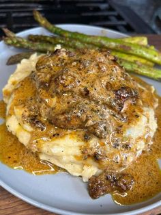 a white plate topped with mashed potatoes covered in gravy and asparagus