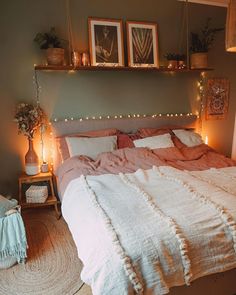 a bed with pink sheets and pillows in a bedroom next to two pictures on the wall