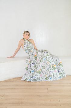 a woman in a floral dress sitting on a white wall and posing for the camera