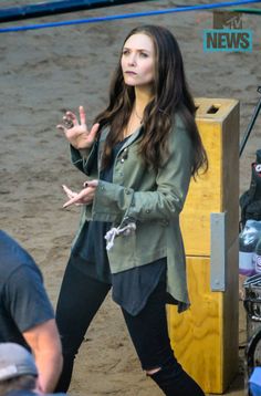 a woman standing on top of a dirt field next to a wooden box with her hands in the air