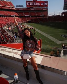 a woman standing on the sidelines of a football stadium with her arms in the air