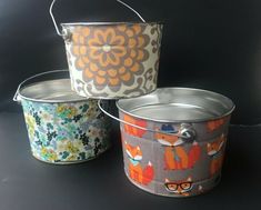 three tin pails with different designs on them sitting next to each other in front of a black background