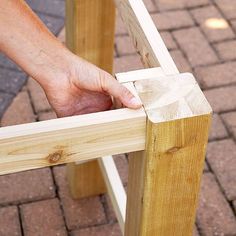 a person holding onto a piece of wood on top of a wooden bench with bricks in the background