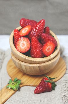 a wooden bowl filled with strawberries on top of a table