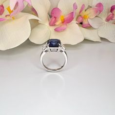 a ring with a blue stone surrounded by white orchids on a table next to flowers