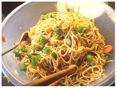 a bowl filled with noodles and vegetables next to chopsticks on a table top