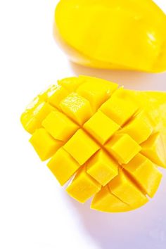 two pieces of mango sitting next to each other on a white surface with one cut in half