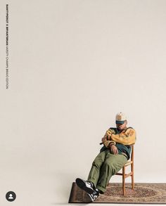 a man sitting on top of a wooden chair in front of a white wall,