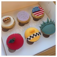 six cupcakes decorated with different designs and colors in a box on a table