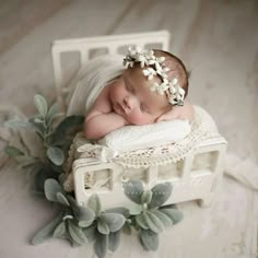 a baby sleeping on top of a white bed next to green plants and flowers in it's hair