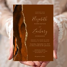 a person holding up a brown and gold wedding card