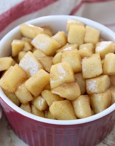 a red bowl filled with sliced apples on top of a white and pink table cloth