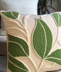 a green and white pillow sitting on top of a couch next to a plant pot