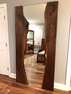 a large wooden mirror in the middle of a room with hardwood floors and white walls