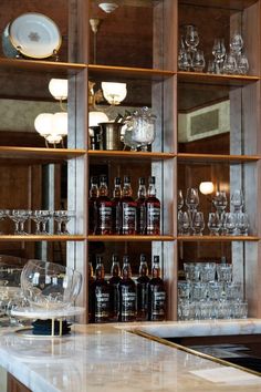 bottles and glasses sit on shelves in a room with marble counter tops, glassware and plates