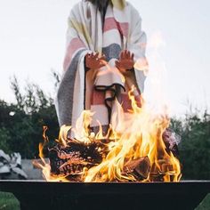 a person sitting in front of a fire pit with their hands on the top of it