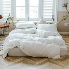 an unmade bed with white sheets and pillows in a room next to a window