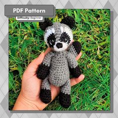 a hand holding a small crocheted raccoon stuffed animal in the grass