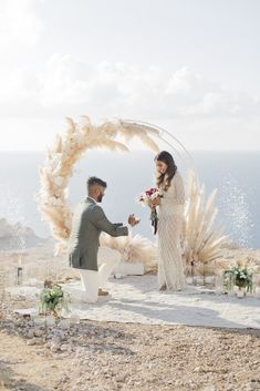 a man kneeling down next to a woman on top of a hill near the ocean