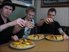 three men sitting at a table with plates of food