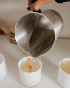 a person pours some liquid into three cups