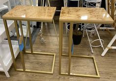 two side tables made out of wood and gold metal frames on display in a store