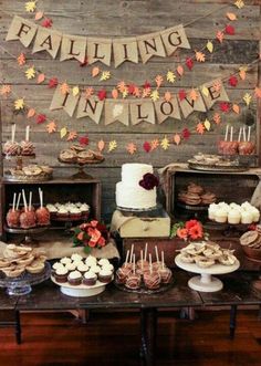 a dessert table filled with cakes and cupcakes on top of wooden tables covered in fall leaves