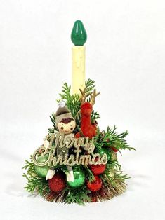 a small christmas tree with a candle and decorations on it's top, in front of a white background