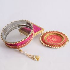 a pink and gold decorated mirror sitting on top of a white table next to a small tray