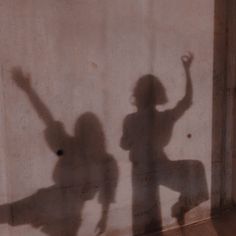 the shadow of two people standing in front of a wall with their hands up and arms raised