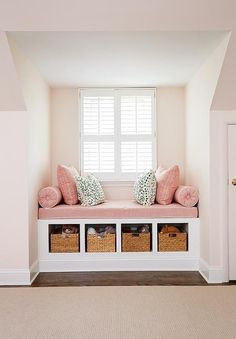 a white window seat with pink pillows and baskets on it in the corner of a room