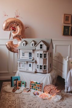 a doll house on top of a bed next to balloons and other items in front of it