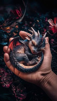 a hand holding a small toy dragon in it's right hand, surrounded by flowers